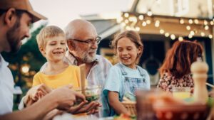 Grandfather and two grandkids enjoying a meal outdoors with whole family