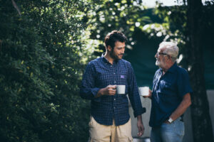 An adult man and his senior father walk and talk as they enjoy a cup of coffee