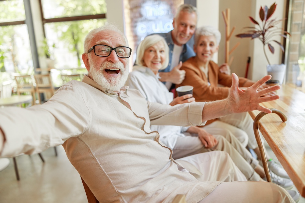 A joyful senior man holds out his arms to welcome other residents at his San Juan Capistrano memory care community