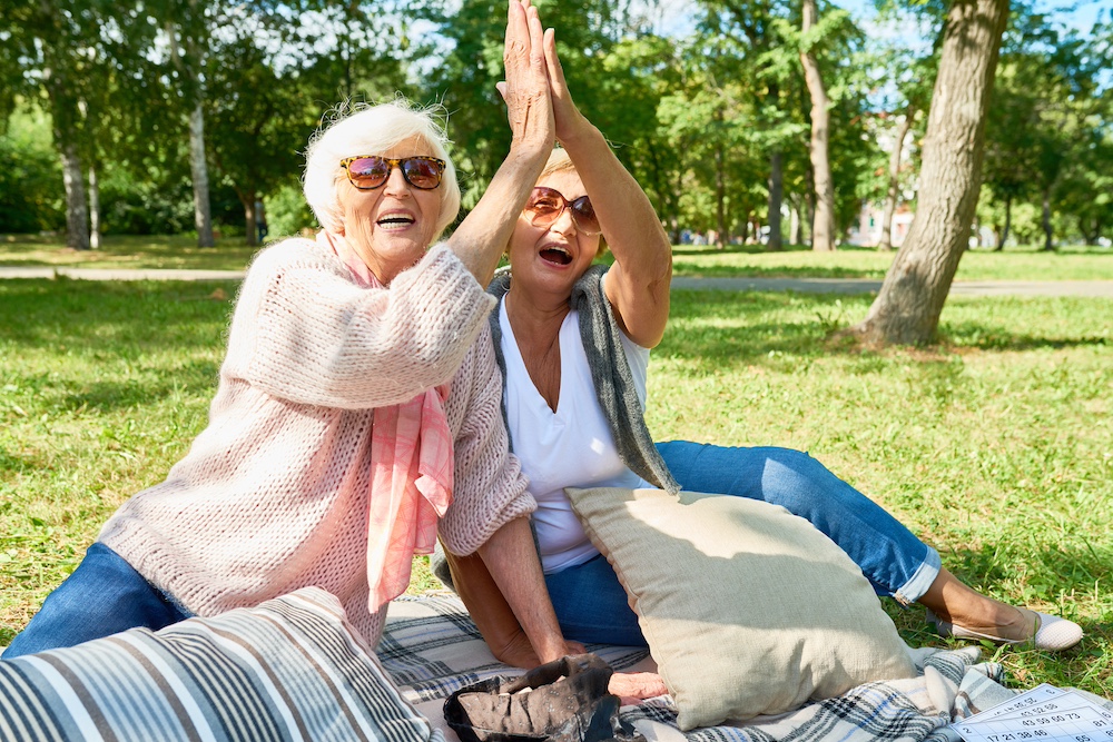 Two senior women share a high five while sitting outdoors