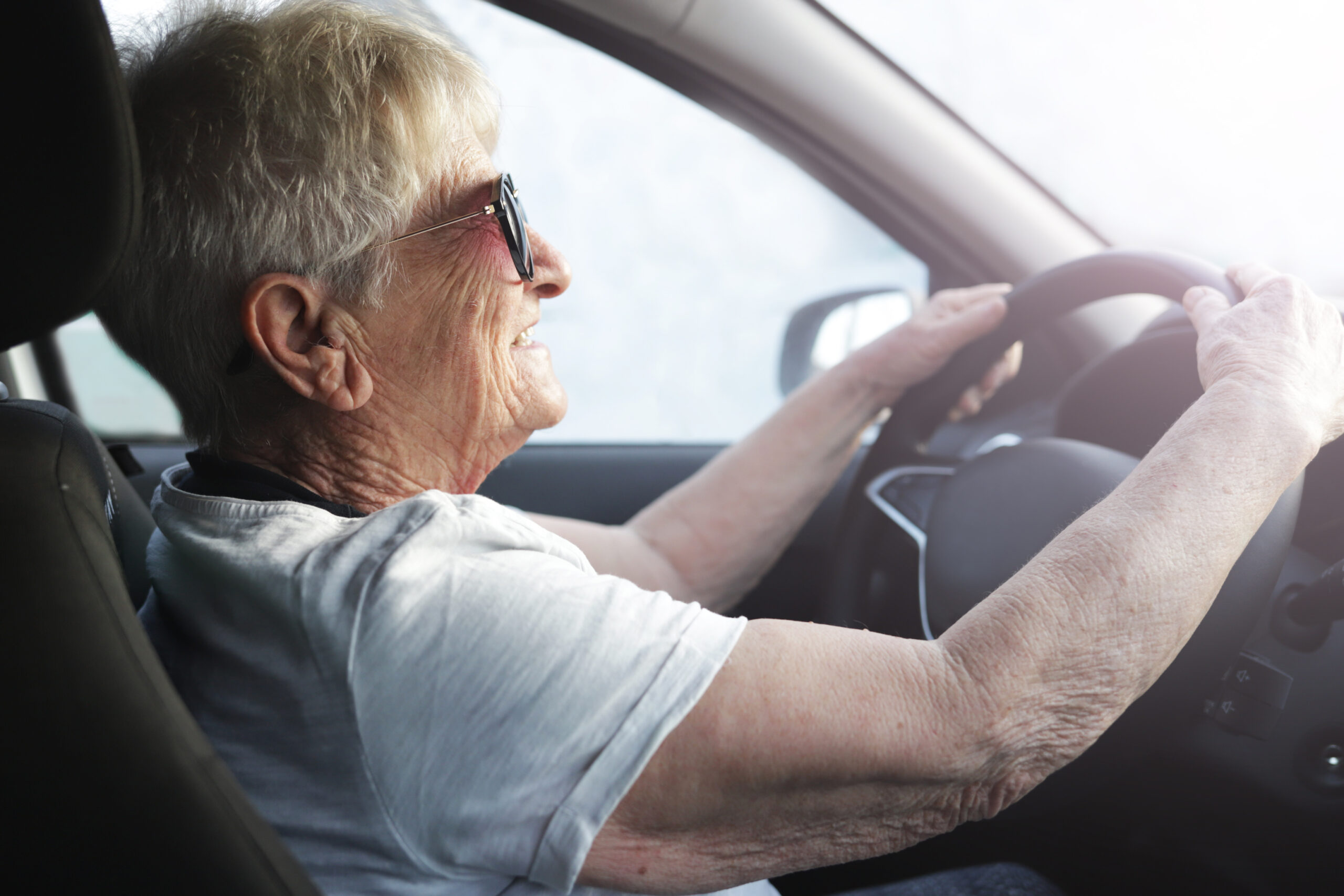 Senior woman driving car wearing sunglasses